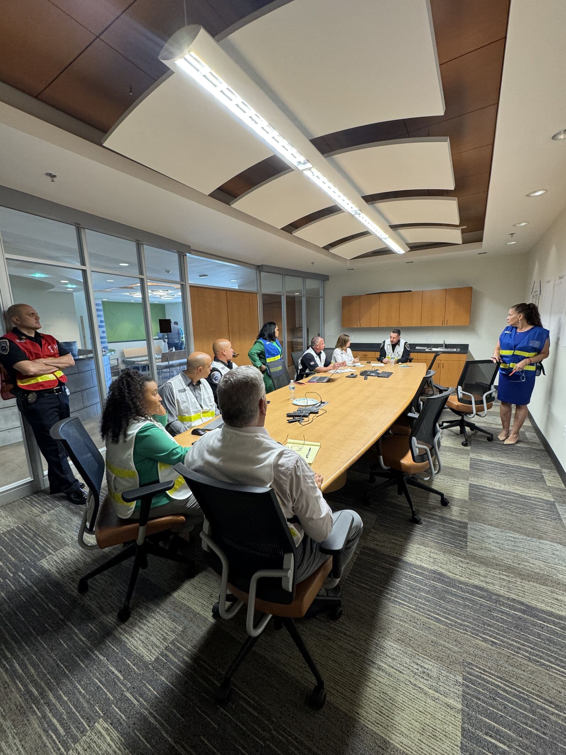 A briefing in a conference room, one person standing to address colleagues seated along a long table