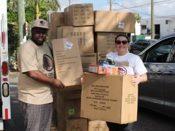 Two people standing beside a stack of large cardboard shipping cartons at the open back of a truck