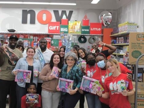 A group of adults and children inside a retail store, most of them holding boxed toys