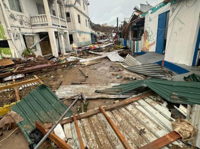 A street covered in sheets of corrugated metal, broken timber and debris between damaged buildings
